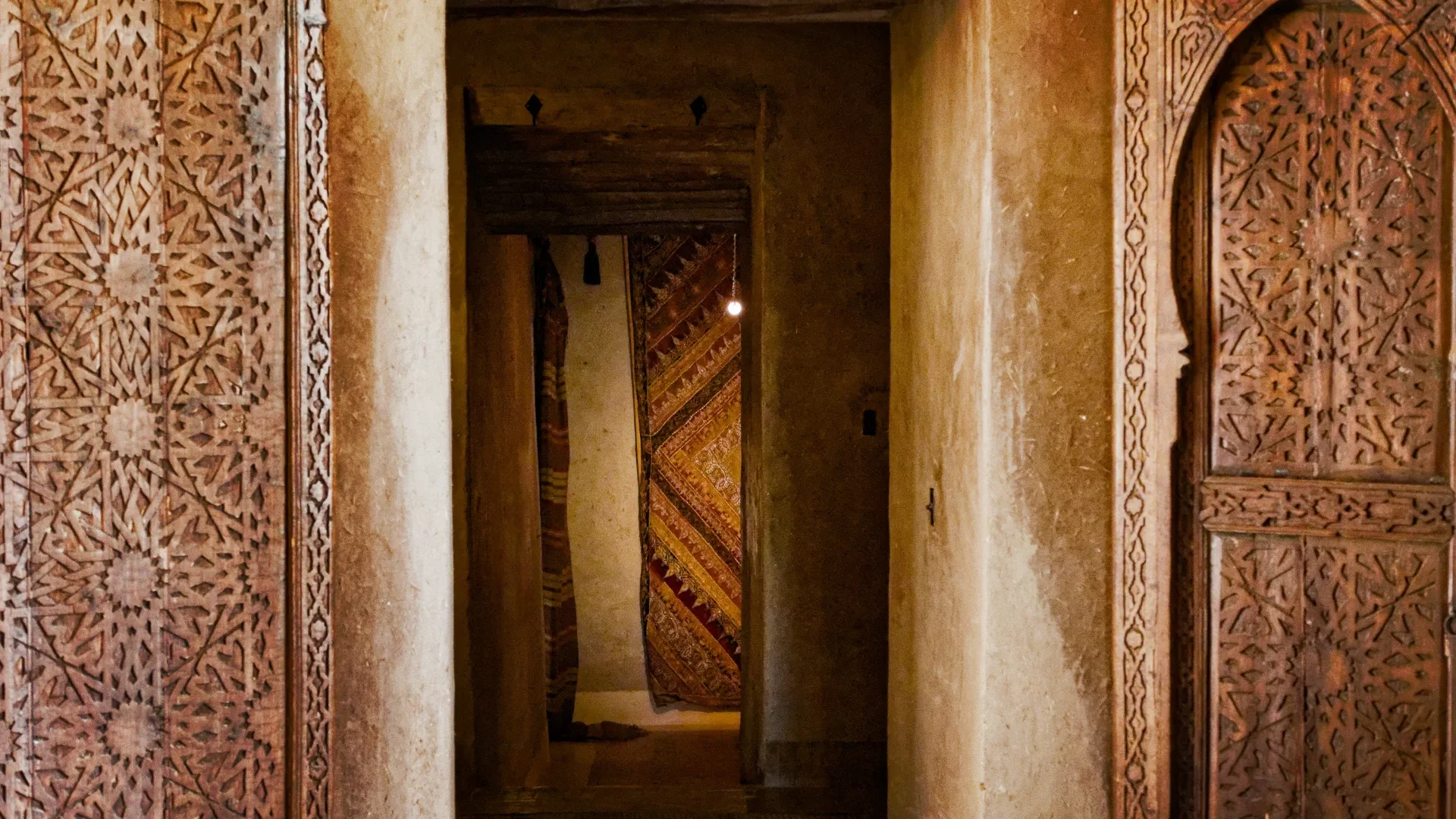 Porte en terre sculptée et étoffes superposées à l'intérieur de Dar Ahlam